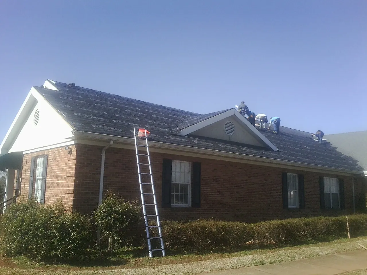 Crew tearing shingles off a brick ranch roof with a ladder set — Emergency Roof Repair work by our crew in Perry