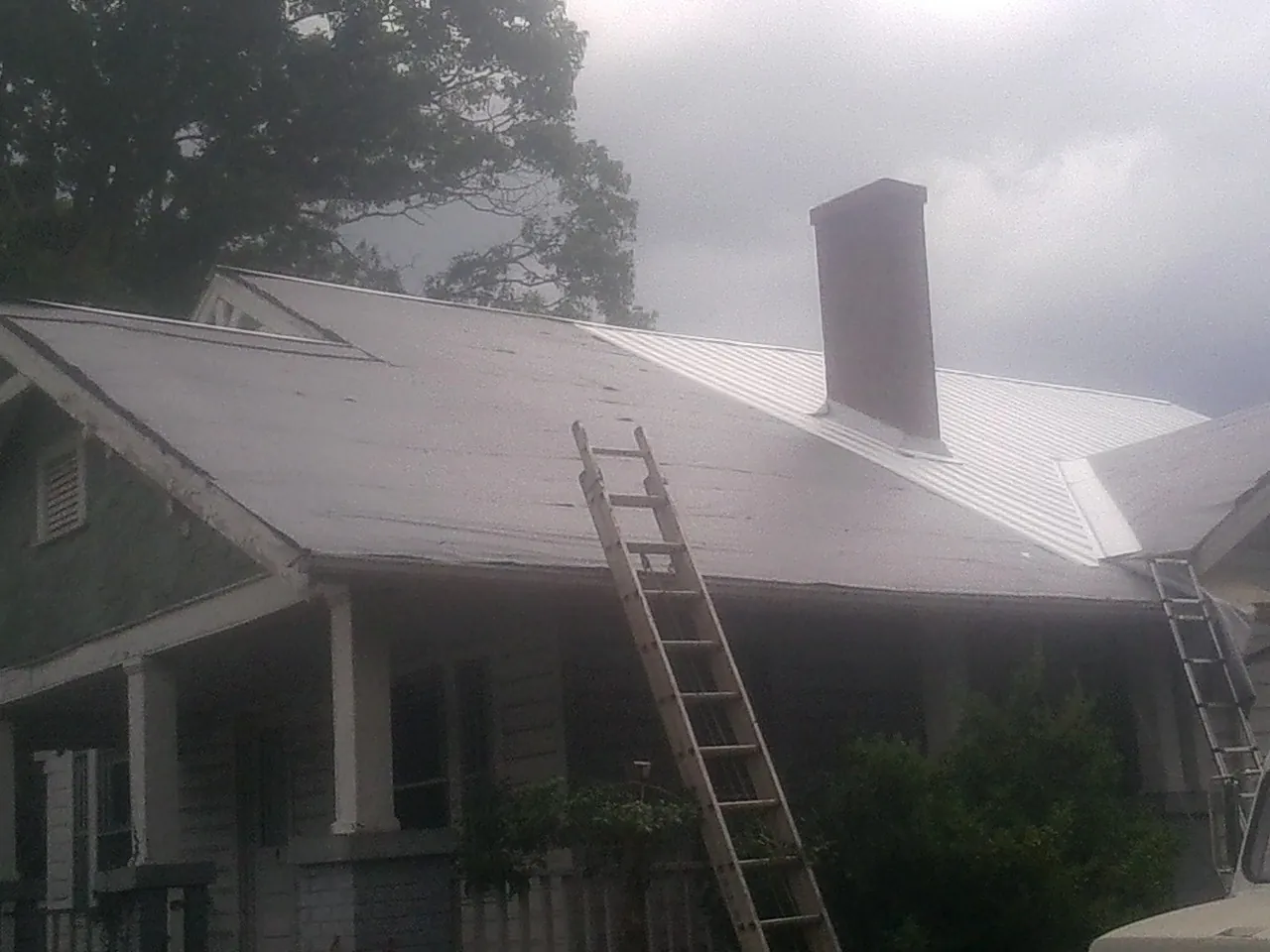 Ladders against a metal roof on an older home with a brick chimney in Perry
