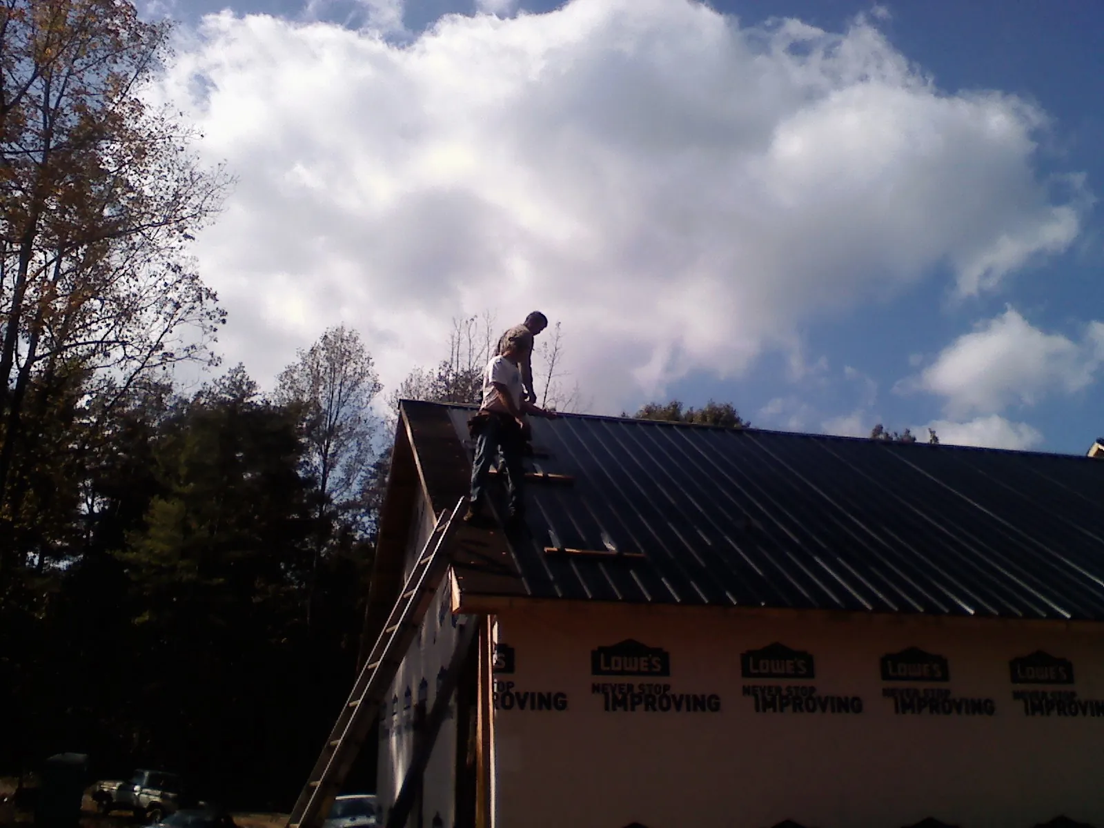 Roofer fastening dark metal panels high against a cloudy sky, from a Roof Inspection job in Perry